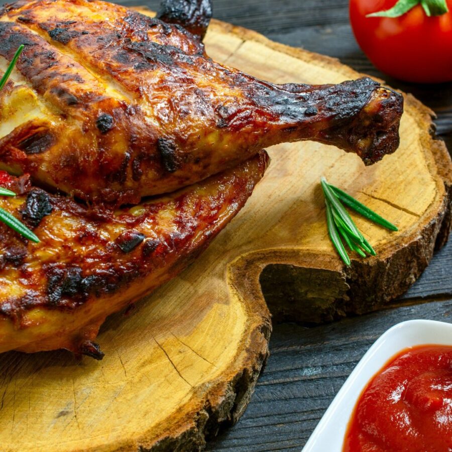Baked part of tasty chicken, with golden brown crust, cooked on grill or barbecue on wooden table.