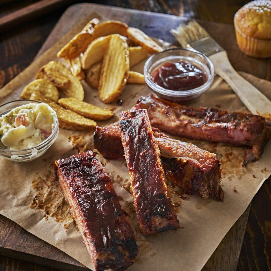 barbecued pork spare ribs with fried potato wedges and cole slaw on parchment paper.
