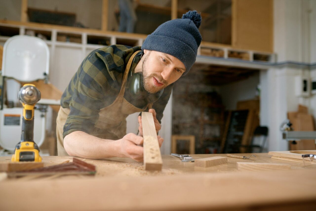 Young man carpenter blowing sawdust from board wooden plank