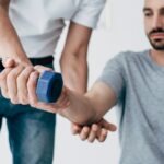 chiropractor stretching arm of patient with dumbbell on grey