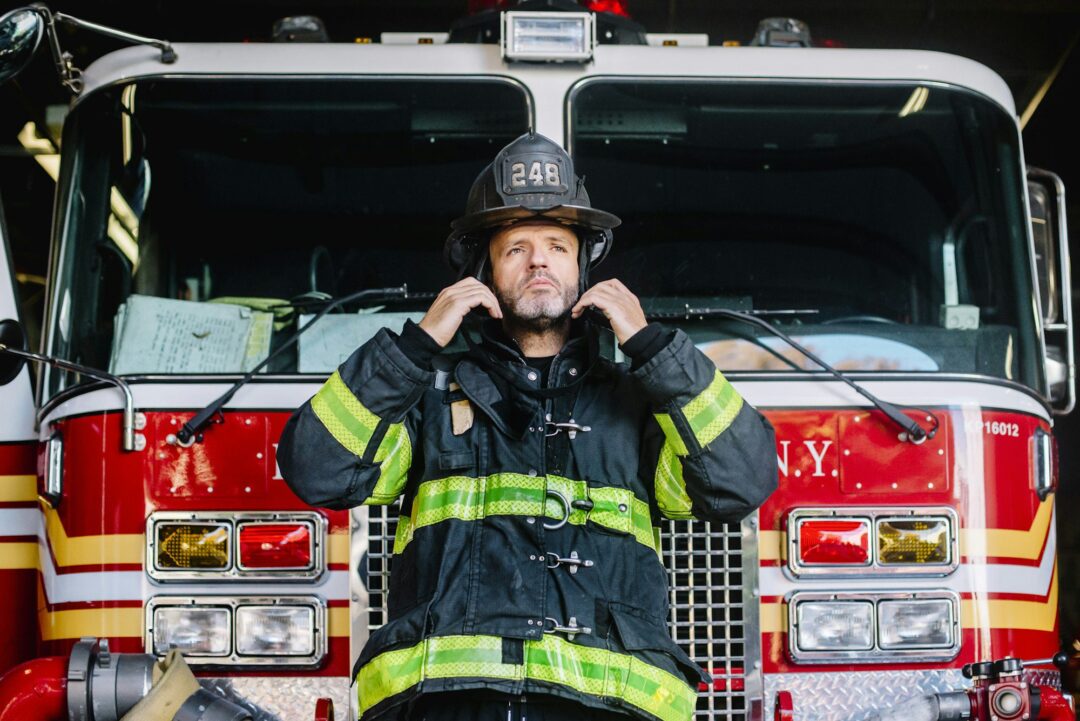 USA, New York, Portrait of firefighter putting on helmet in front of fire engine
