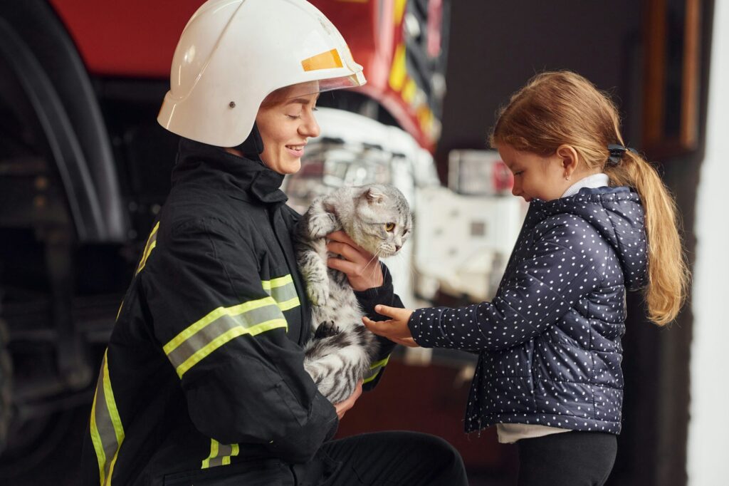 Rescued scottish fold cat. Firefighter woman in uniform is with a little girl