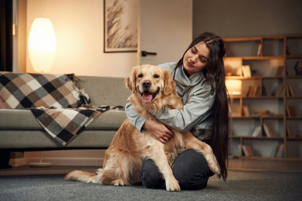Sitting and smiling. Woman is with golden retriever dog at home
