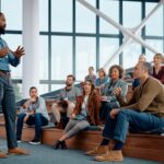 Black businessman talking to large group of entrepreneurs during education event in conference hall.