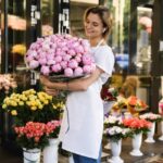 Woman florist with a heap of pink peony flowers in her little flower shop