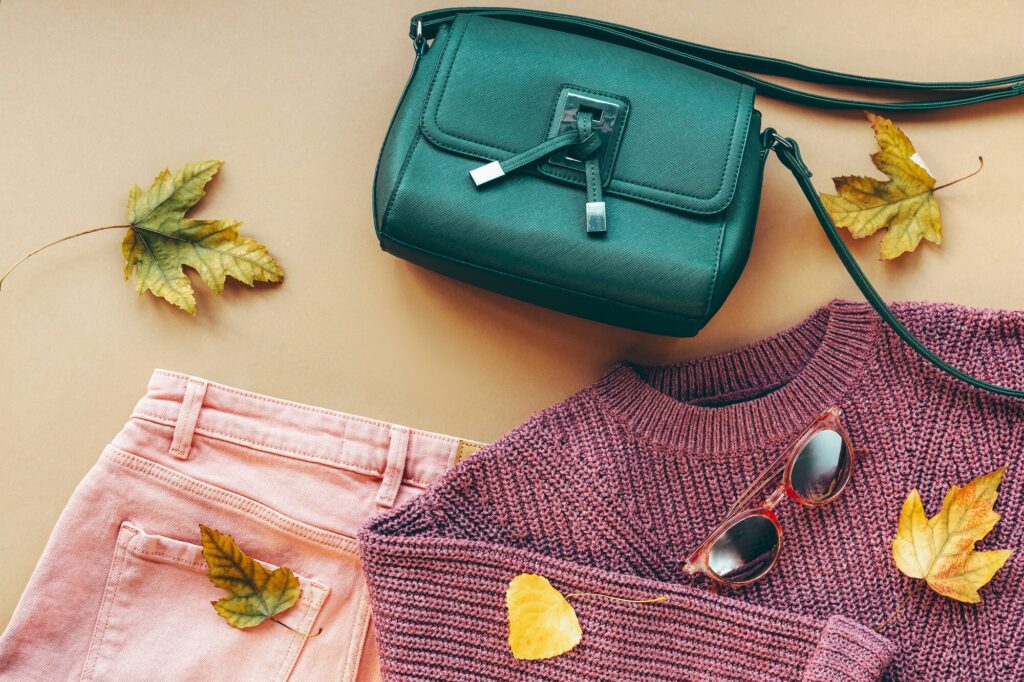 Flat lay of woman's apparel, fashion trend. Beige background with autumn leaves, sweater and jeans