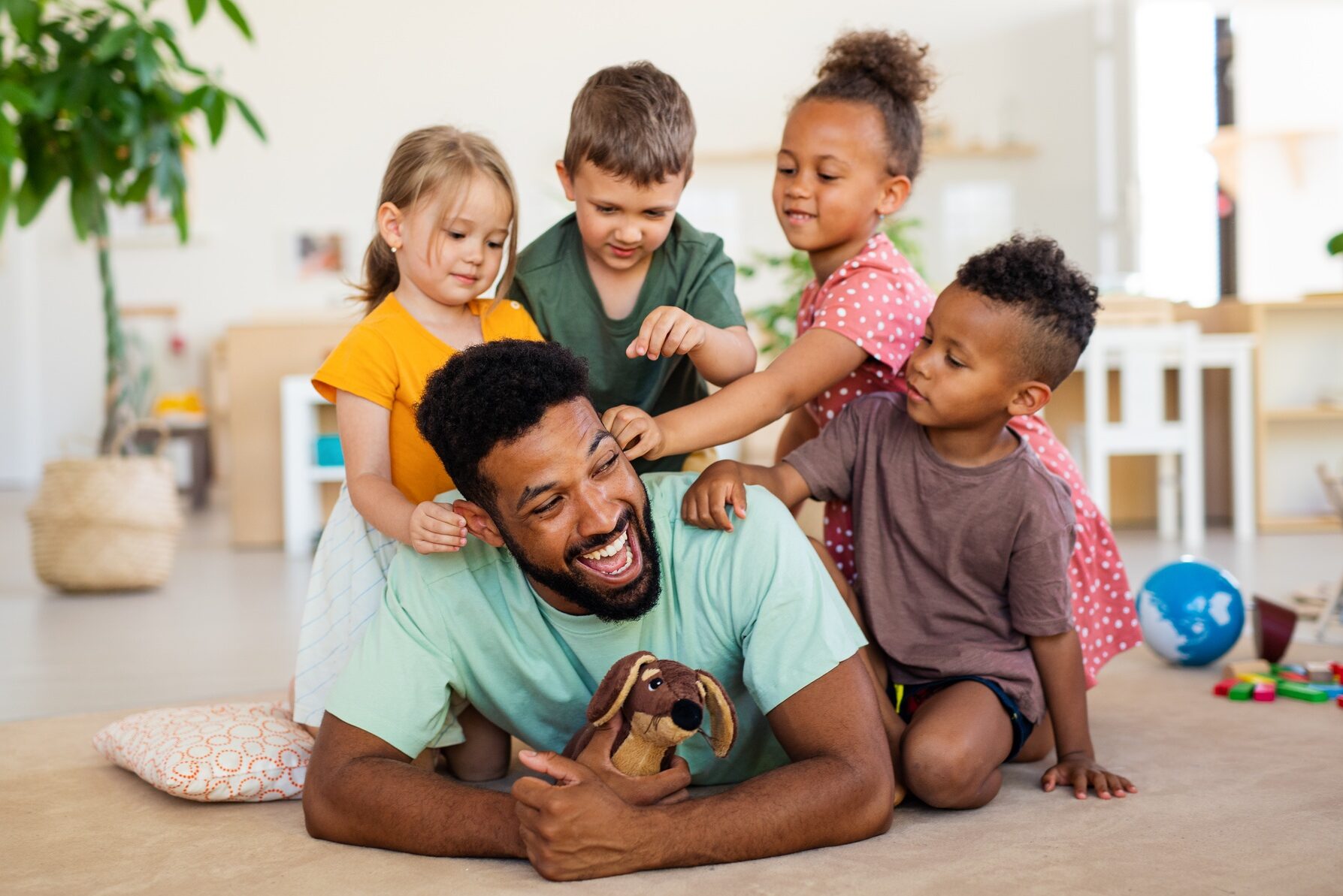 Nursery school children with man teacher sitting on floor indoors in classroom, playing.