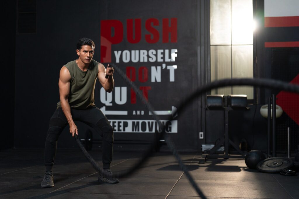Fit Asian man in sportswear exercise with battle ropes at gym fitness center