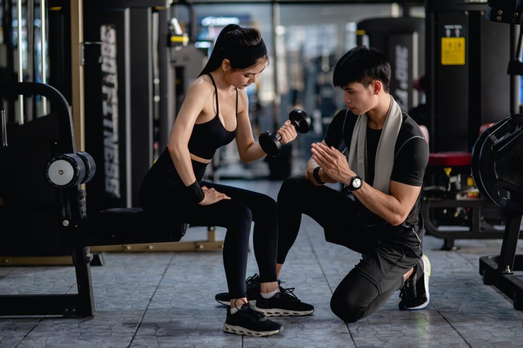Young fitness woman exercise with dumbbell by trainer in gym.