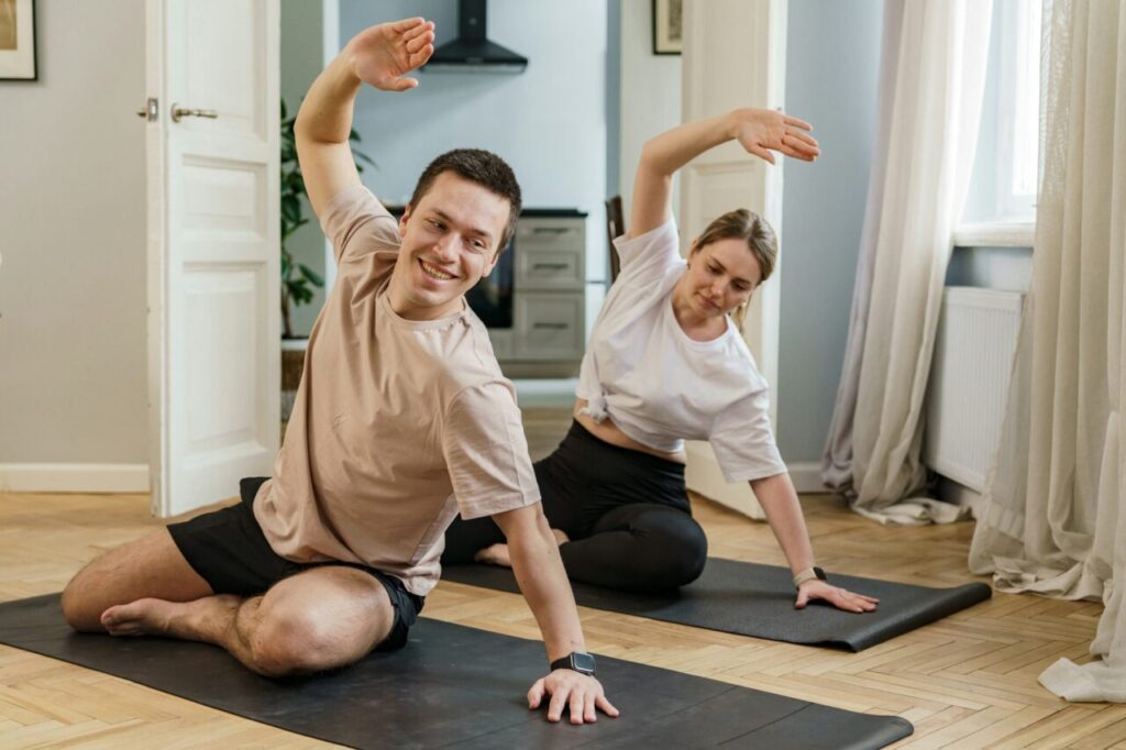 Couple joyfully stretching on yoga mats at home, sharing a moment of fitness and wellness