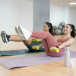 TWO GIRLS TRAINING YOGA AND PILATES TOGETHER WITH A BALL AND WEIGHTS
