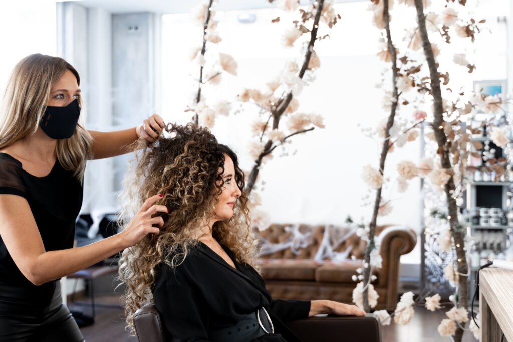 Hairdresser fixing the curly hair of a woman in front of a mirror in a salon